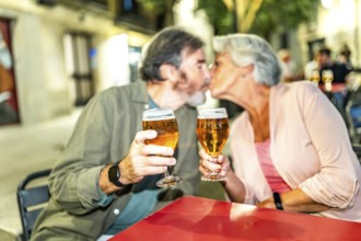 Senior couple kissing while toasting with beer in an outdoor terrace in the city
