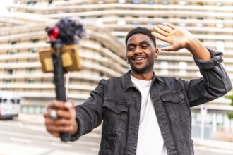 Young African man waving while filming a video blog in the city