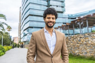 Frontal portrait of a Latin smiling businessman with hands on pockets standing proud outdoors in