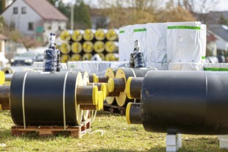 Stacked district heating pipes and district heating lines with yellow ends lie piled up in a meadow