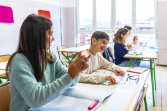 Happy elementary school students clapping hands in classroom, enjoying learning and having fun at