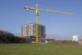 Building under construction behind overgrown hill, with crane and clear sky, residential