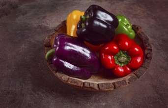 A collection of colorful bell peppers, in a wooden bowl, on a dark surface, top view, no people