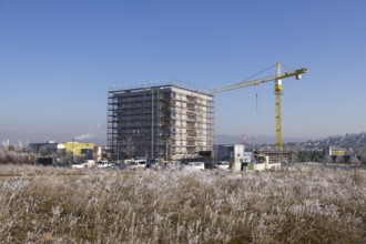 Open field with high-rise building under construction and crane, clear winter sky, housing