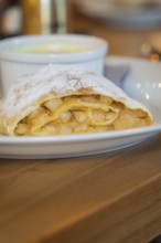 Close-up of an apple strudel with icing sugar and visible apple pieces on a plate, autumn creations