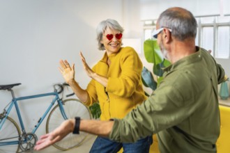 Modern senior couple with stylish sunglasses having fun together at home laughing and dancing