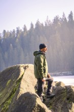 Man with outdoor clothes standing on a rock, surrounded by forest and sunlight, Glaswaldsee, Bad