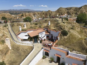 A white house with terracotta roof on a hill surrounded by nature and some people enjoying the