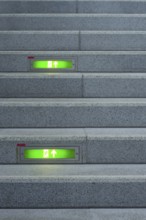 Public staircase with green illuminated emergency exit signs, Germany, Europe