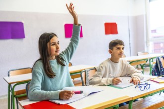 Girl raising hand to answer a question during class in elementary school while her classmate is