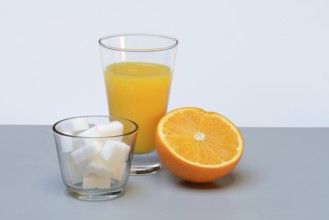 Orange juice in a drinking glass, half an orange and sugar cubes