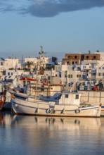 Fishing boats in the harbour at sunset, reflected in the sea, White Cycladic houses, Naoussa,