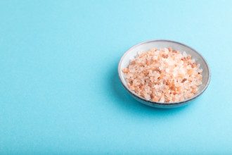 Plate with pink Himalayan salt on blue pastel background. side view, copy space