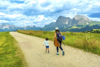 Mother and son walking on a path in alpe di siusi, dolomites, enjoying summer vacation in italy