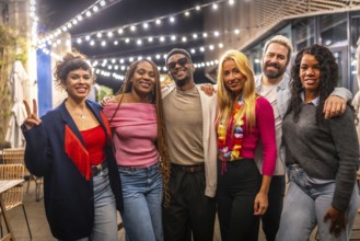 Portrait of multi-ethnic young friends standing smiling at camera in a bar terrace at night
