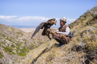 Traditional Kyrgyz eagle hunter with eagle in the mountains, near Kysyl-Suu, Kyrgyzstan, Asia