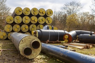 Stacked district heating pipes with yellow ends lie piled up in a meadow