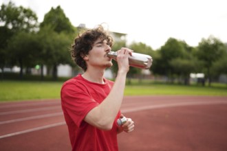 Thirsty caucasian young amle athlete drinking water in a reusable bottle after training in a