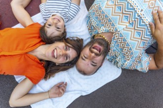 A family of three, a man, a mother and a son, are laying on a blanket on the ground. The man is
