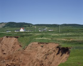 Cliff with eroded soil and houses in the distance in summer, Havre-Aubert, Magdalen Islands,