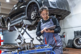Young woman mechanic using a digital tablet, inspecting car parts and components in a professional