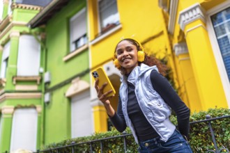 Low angle view photo of a cool afro young woman in urban clothes listening to music next to