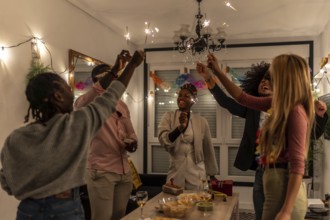 Multi-ethnic happy friends raising burning sparkler celebrating party at night at home