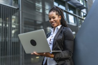 Hispanic confident businesswoman working with laptop standing outside a modern building