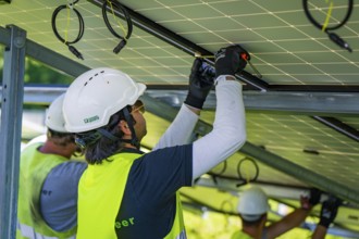 Workers install solar panels wearing safety helmets and high-visibility waistcoats, construction of