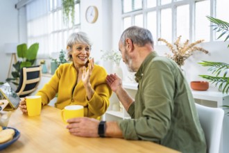 Lovely mature couple enjoying morning coffee at home sitting on living room table and chatting