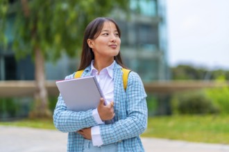 Dreamy chinese student standing outside the university looking away with proud look