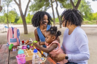 Happy african girl playing with toys sitting in a park with her mother and grandmother