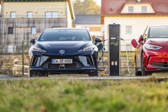 A black electric car being charged next to a charging station in a rural area, Deer E- Carsharing