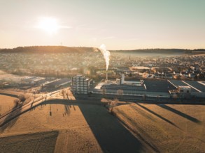 Urban landscape with factory and smoke, surrounded by fields at sunset with long shadows,