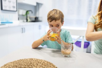School boy drinking orange juice at home with his mother at the side before going to school