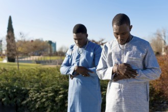 Two young senegalese muslim men wearing traditional dashiki clothing are performing salat prayer