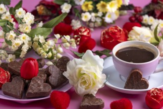 Coffee mug with chocolate and flower arrangement on a pink background, Valentine's Day