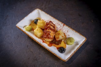 Octopus tentacle with potatoes on a black background, on a white plate