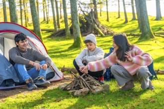 Brother and dad preparing bonfire next to camping tent in an alpine forest