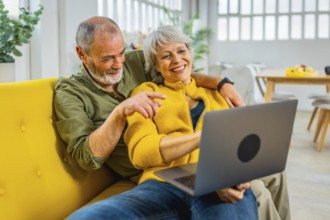 Mature woman lying on her husband sharing laptop on sofa in a cozy modern apartment