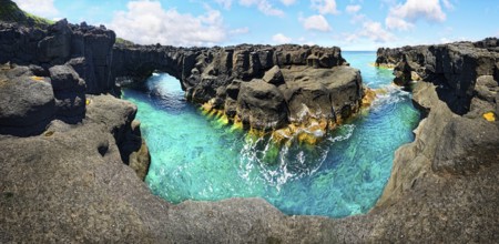 Panoramic view of rugged lava rock formations with a natural arch over turquoise sea under blue