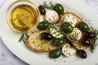 A plate with a snack, ciabatta bread with cheese and olives, olive oil, spices and herbs, top view,