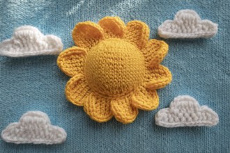Crocheted yellow sun and white clouds on a light blue knitted background, AI generated, AI