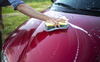 Close-up of a hand washing the hood of a red car with a sponge and soap