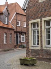 Paved village street with old brick buildings and blooming flower box, Legden, münsterland,