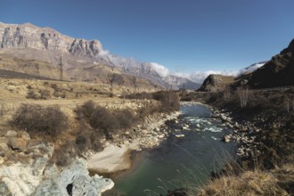 A mountain river in a mountainous rocky area near which there are power lines on the background of