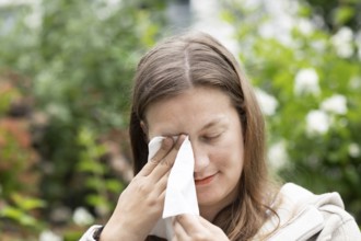 Young woman suffers from hay fever and uses a paper handkerchief outdoors, Freiburg,