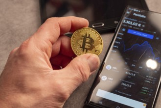 A hand shows a Bitcoin coin next to a smartphone with portfolio data