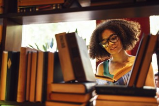 Happy African American female student studing in university library and looking for the book,