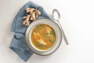 Healthy soup from chicken meat, vegetables and ginger in a bowl on a blue napkin and a gay white
